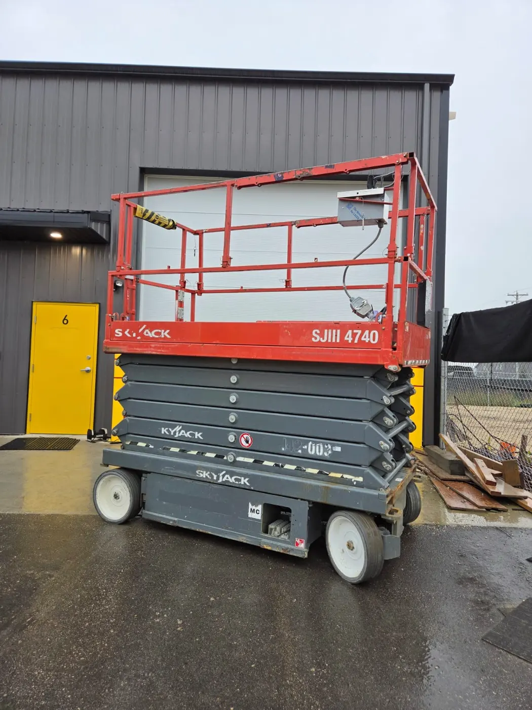 Red Skyjack electric scissor lift from the side, platform lowered