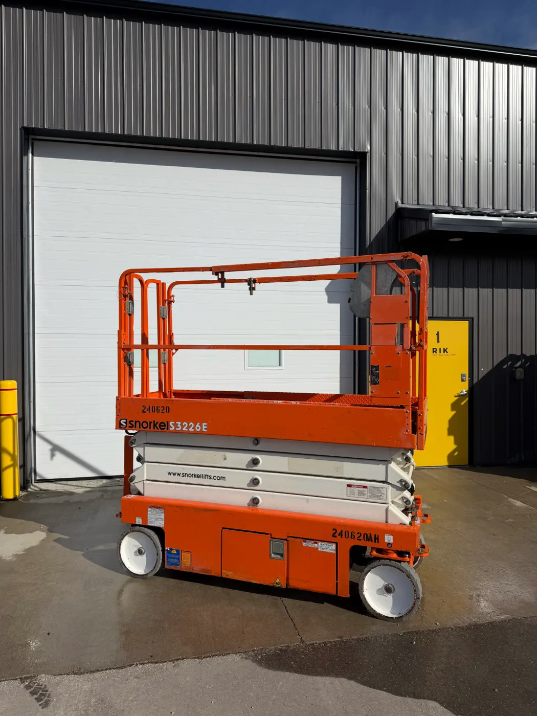 Orange Snorkel electric scissor lift from the side, platform lowered